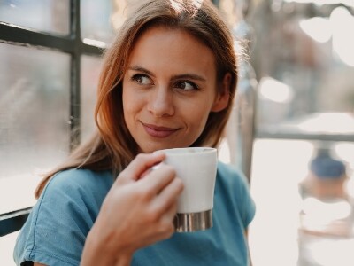 woman wearing blue drinking coffee beside window